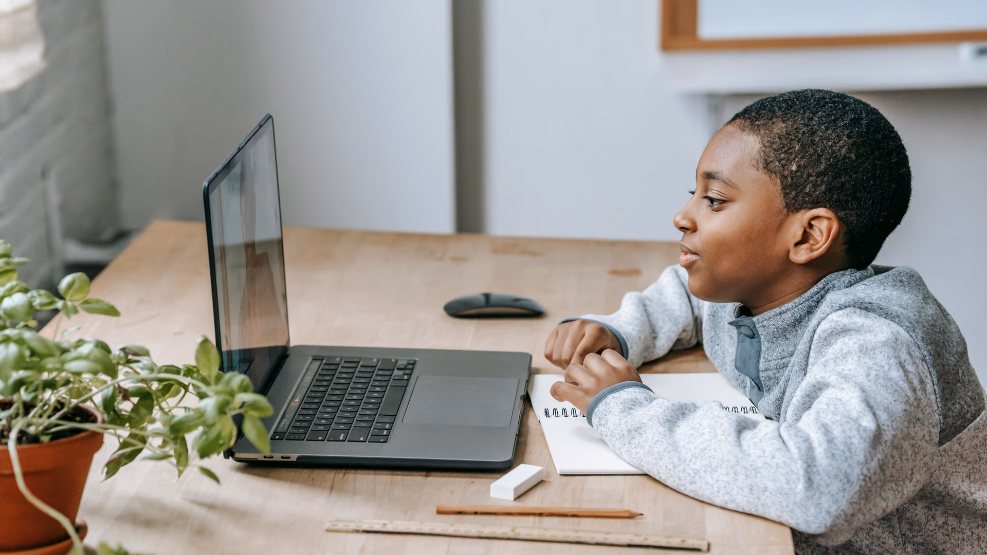 A young boy focused on online learning at home, using a laptop and notebook, illustrating modern education - Image by Katerina Holmes from Pexels