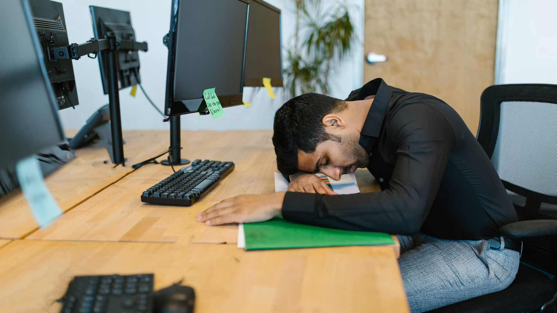 An exhausted office worker resting on a desk surrounded by computer monitors in a modern workspace - Image by RDNE Stock project from Pexels